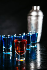 Blue and red cocktails in shots and shaker standing on a bar counter