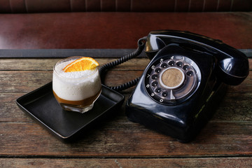 cinema style photo of black dial phone and coffee cocktail with orange peel on wooden table....