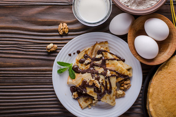 Flat lay French crepes with chocolate sauce walnuts eggs and flour on wooden kitchen table