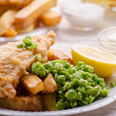 Traditional British street food fish and chips with tartar sauce and mushy peas on paper plate