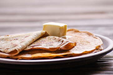 Stack of French crepes with butter in ceramic dish on wooden kitchen table