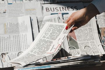 partial view of woman taking daily print newspaper from stand