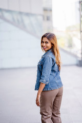 A beautiful,young Malay Asian woman casually dressed but stylishly. She is standing by the street in the city during the day. She is wearing a denim jacket and pants as she show her lovely smiles. 