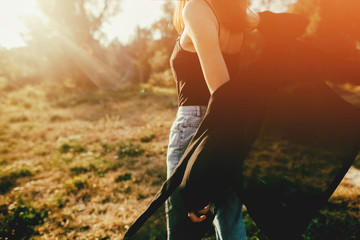 Stylish hipster girl having fun in sunny park in amazing sunbeams, atmospheric moment. Fashionable cool woman dancing and smiling in evening light. Selective focus. Retro effect. Creative image