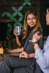 A beautiful, fashionable, millennial Asian Malay businesswoman having a discussion with her colleague by her side. They are sitting in a cafeteria and having a cold beverage during the day.