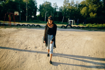 Stylish hipster girl walking in sunny street, atmospheric moment. Fashionable cool woman with black sunglasses and denim jeans relaxing at playground. Selective focus. Retro effect