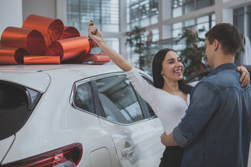 Excited young couple hugging, celebrating buying new automobile together at car dealership....