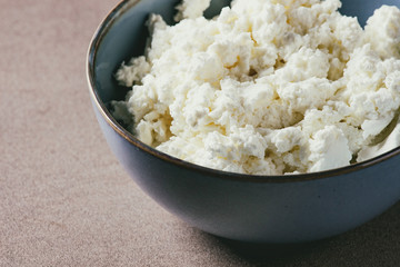 Fresh organic cottage cheese in blue ceramic bowl on brown texture background.Close up, space