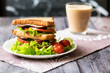 Sandwich with cheese, tomato, cucumber, sausage and lettuce on a wooden background. Vertical orientation