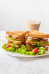 Sandwich with cheese, tomato, cucumber, sausage and salad on a light background. Coffee with milk. Vertical orientation