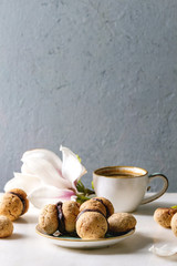 Baci di dama homemade italian hazelnut biscuits cookies with chocolate cream served in ceramic plate with cup of espresso coffee and magnolia flowers over white marble table. Copy space