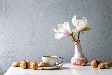 Baci di dama homemade italian hazelnut biscuits cookies with chocolate cream served in ceramic plate with cup of espresso coffee and magnolia flowers over white marble table. Copy space © Natasha Breen