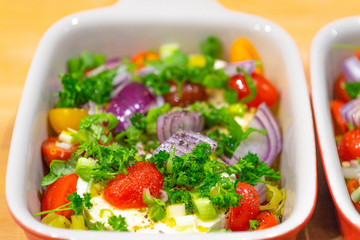 Large portion of ripened Halloumi or Feta cheese with many fresh herbs, tomatoes and red onions in a casserole dish for grilling in the oven or on the grill for a barbecue