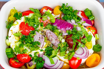 runder schafskäse mit gelben und roten tomaten, frühlingszwiebeln, roten zwiebeln, Peperoni, Olivenöl und frischen kräutern wie Petersilie, Basilikum und Kresse in einer kleinen auflaufform