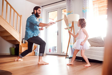 A small girl and young father with paper swords at home, playing.