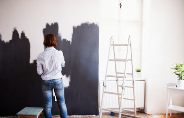 A rear view of young woman painting wall black. A startup of small business.