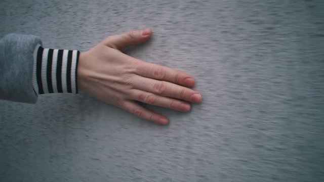 Camera follow close up of human hand touches grey concrete wall, fingers stroking scabrous surface of building.