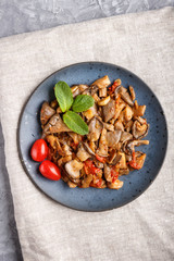 Fried oyster mushrooms with tomatoes on gray concrete background. Top view.