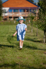 Little girl in a dress in the style of country music in the summer garden on the background of country house