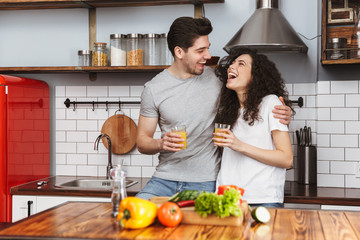 Portrait of optimistic couple cooking salat with vegetables together while having breakfast in kitchen at home