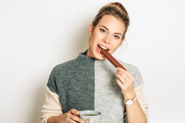 Pretty young woman eating chocolate bar, studio image taken on white background