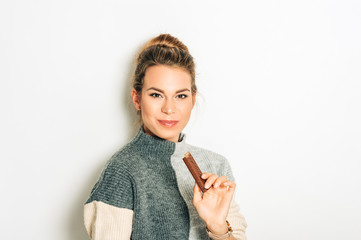 Pretty young woman eating chocolate bar, studio image taken on white background