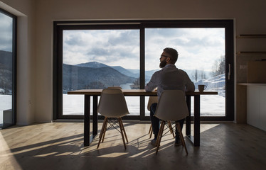 Rear view of mature man sitting at the table in new home, using tablet.