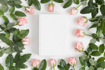 Top view of a white book mockup surrounded by pink roses on a white table.