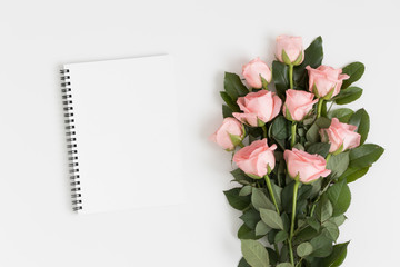 Top view of a white notebook mockup with a bouquet of pink roses on a white table.