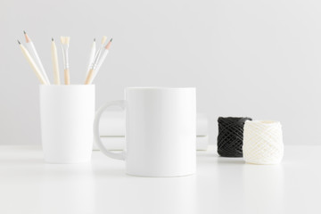 Naklejka premium Mug mockup with workspace accessories on a white table.