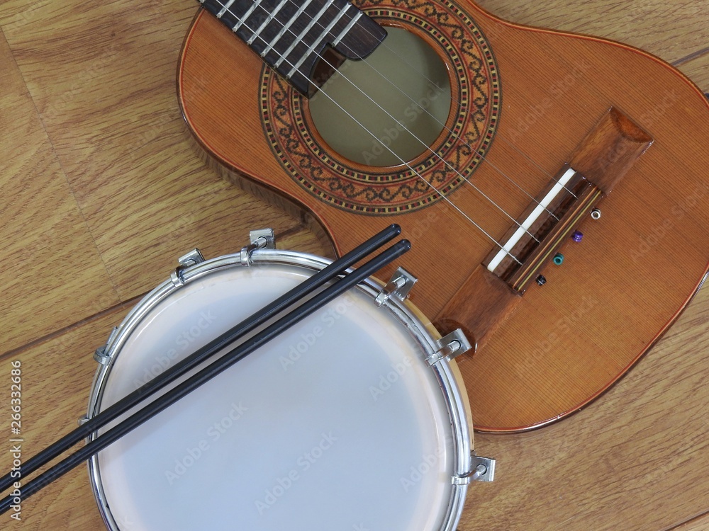 Wall mural Close-up of two Brazilian musical instruments: cavaquinho and tamborim with drumstick on a wooden surface. They are widely used to accompany samba music.