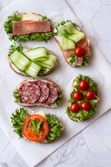 Fresh sandwiches with sausage, cheese, bacon, tomatoes, lettuce, cucumbers on a light background....