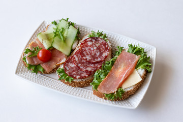 Fresh sandwiches with sausage, cheese, bacon, tomatoes, lettuce, cucumbers on a light background. Horizontal orientation