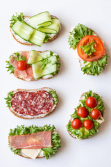 Fresh sandwiches with sausage, cheese, bacon, tomatoes, lettuce, cucumbers on a light background....