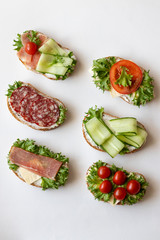 Fresh sandwiches with sausage, cheese, bacon, tomatoes, lettuce, cucumbers on a light background....