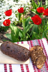 Rye bread on a wooden board against the background of spring flowers. fresh bread on a background of blooming tulips