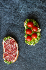 Fresh sandwiches with sausage, cheese, bacon, tomatoes, lettuce, cucumbers on a dark background....