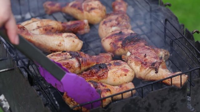 Barbecue Chicken Legs. Woman turns over the hot smoking roasted chicken wings on the barbecue for the good roasting, BBQ at the backyard in the. Green summer day, cooking outdoors on