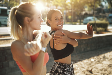 Two fit women smiling and stretching before an outdoor run