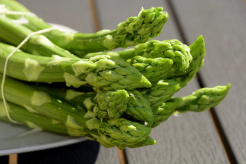 unusual macro shot of asparagus officinalis, a bundle of washed raw garden asparagus or sparrow grass on plate lit by the sun abstract look