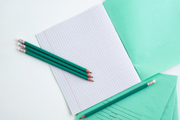 On the table is an open notebook in a cage. Pencils next to the school notebook. Notebook for schoo