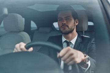 Looking forward. Handsome young man in full suit looking straight while driving a car