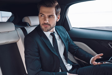 Fototapeta na wymiar Young and successful. Handsome young man in full suit looking away while sitting in the car