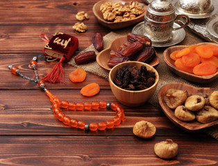 Ramadan concept. Delicious dates, dried figs, dried apricots, walnuts, almonds, raisins on bamboo and silver plates, rosary beads with Islamic holy book Quran on a pine wooden table background.