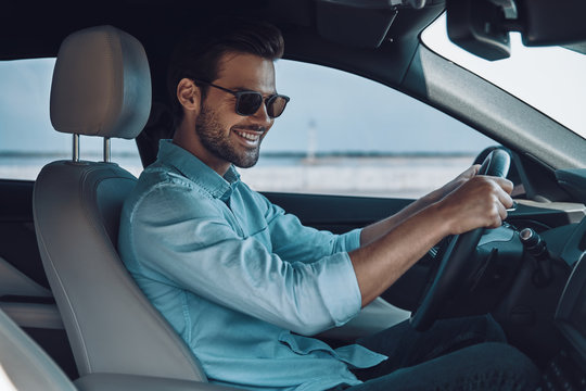 Happy To Drive New Car. Handsome Young Man In Smart Casual Wear Smiling While Driving A Status Car