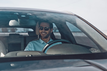 Convenience way to travel. Handsome young man smiling while driving a status car