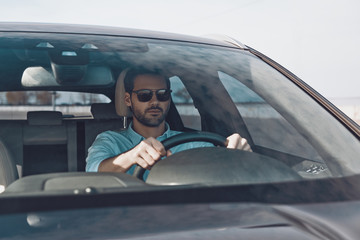 Driving carefully. Handsome young man looking straight while driving a status car