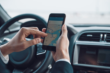 Checking the direction. Close up of young man using smart phone to check the map while driving a car