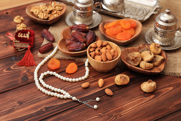 Ramadan concept. Delicious dates, dried figs, dried apricots, walnuts, almonds, raisins on bamboo and silver plates, rosary beads with Islamic holy book Quran on a pine wooden table background.