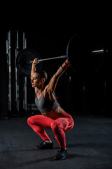Young, European, muscular girl in red leggings, doing exercise with a barbell in the gym for...
